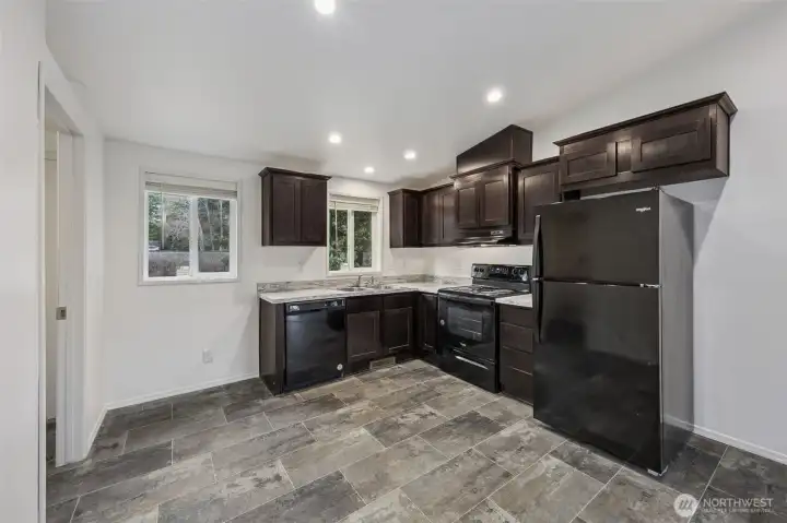 A kitchen that understands function and style can coexist. The dark shaker cabinetry sets a strong tone, paired with Formica countertops that prioritize durability over drama. Black appliances keep things streamlined, while the stone-look vinyl flooring offers easy maintenance with a polished finish. There’s space for a dining table or a cozy breakfast nook beneath the window, and the sink overlooks the backyard for a little everyday scenery. Located right next to the utility and pantry area, the layout works hard without feeling busy.