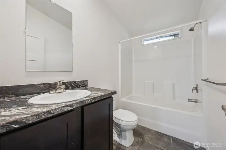 This main full bathroom in located next to bedrooms #2 & #3 and balances smart finishes with clean design. The tub surround mimics white tile with a textured surface that’s easy to maintain and surprisingly polished. Formica counters get a quiet win here, durable, budget-smart, and resistant to everyday wear, which means less worrying and more living. Stone-look vinyl floors handle moisture like a pro, brushed nickel hardware keeps things timeless, and the vaulted ceiling with a high privacy window brings in light without sacrificing discretion. Functional, fresh, and very low drama.