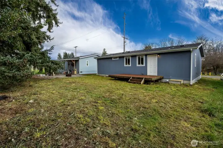 Here’s where the backyard starts to show its potential. The side yard is an ideal spot for a future gate, especially if fencing is on your list. Crawlspace access is conveniently located near the deck, keeping everything accessible but discreet. Add in the level lawn, clear skies, and evergreen backdrop, and you’ve got a yard that feels calm, usable, and easy to live with.