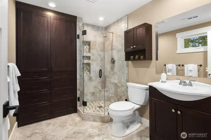 The en suite 3/4 bath is adorned with tile floors, shower, a frameless glass panel shower door, and a large built-in cabinet.