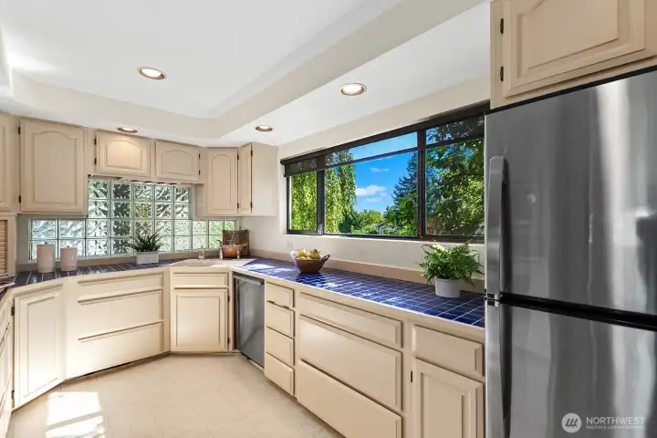 Bright kitchen featuring abundant cabinetry, tile countertops, and large picture window