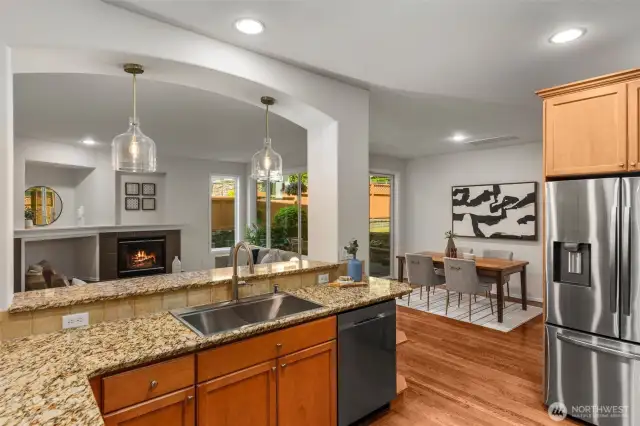 Wrapped in abundant counter space, the modern kitchen features a deep farmhouse-style double sink with elegant swan neck faucet (new 2025),convenient garbage disposal, and a stainless steel dishwasher (new in 2022). An open breakfast bar with pendant lighting connects seamlessly to the living room for easy entertaining and everyday living.