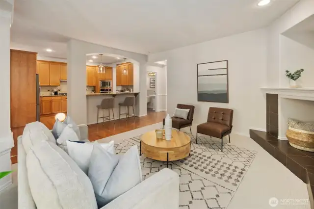 The spacious yet cozy living room features soft carpet underfoot and flows seamlessly into the kitchen, creating a warm sense of connection. An elegant arched opening frames the breakfast bar, inviting conversation between rooms. Detailed columns, rich hardwood floors, recessed lighting, and high ceilings lend a regal feel to this beautifully finished space.