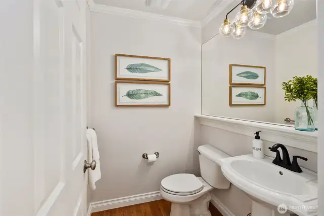 Tucked just off the main hallway between the kitchen and dining room, this elegant powder room features a classic pedestal sink, new faucet, new toilet, updated vanity lighting, and a large wall-to-wall mirror. Warm hardwood floors add a touch of charm to this convenient main-floor space.