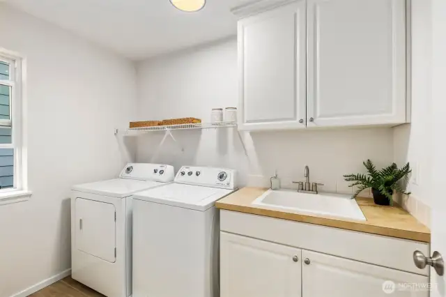 Upstairs near the bedrooms, this spacious laundry room features a Whirlpool washer and dryer (2014), a sink for hand washing, and abundant cabinetry for storage. New LVP flooring adds durability and style, while a large window fills the room with natural light.