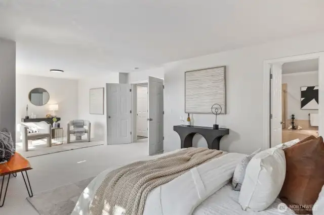 Another view of the expansive primary suite shows double-door entry and direct access to the en suite bath. The sitting area feels like its own peaceful lounge space — beautifully lit by natural sunlight and enhanced by fresh, neutral tones.