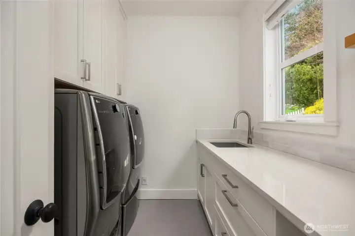 Beyond the kitchen & to the left is a spacious laundry room with abundant custom built-in cabinetry, heated Pental tile flooring, a desk, quartz counters and a high end LG Washer/Dryer plus an additional pedistil washer.