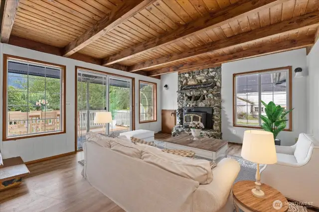 The Family room w/ tongue & groove ceilings, lg beams, woodstove, laminate flooring & a slider to the back deck. Virtually Stage.