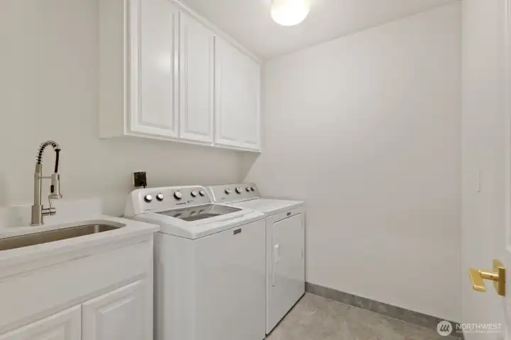 Laundry room on the mail floor with a new tiled floor, quartz utility sink and white cabinets.