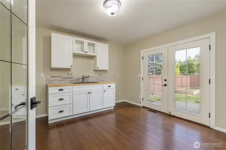 Kitchenette with sink and space for a fridge has French doors leading to the back yard.
