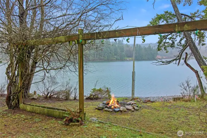 Old vines over an arbor show case the stone fire pit at the beach.