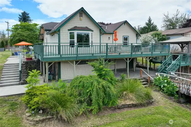 There is another patio area on the left, accessed by the yard or the upper deck, with stairs leading to the lower patio and pool area.