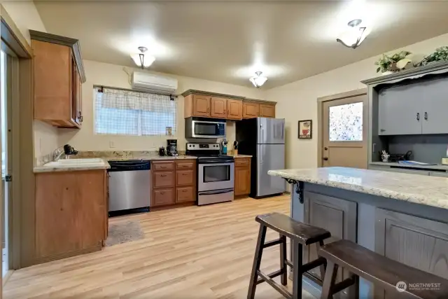 The kitchen in Unit A has a back door that leads to the fenced parking area. Extra storage in the hutch behind the island. The bathroom & laundry room are on the left.