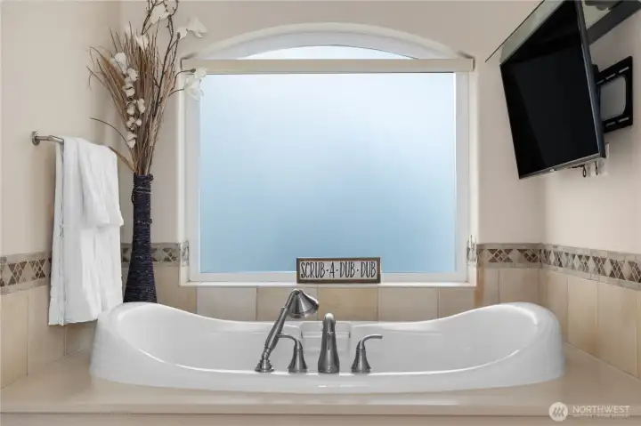 The soaking tub is framed by tile detail, privacy glass, and a spa-like setting.