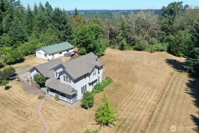 Aerial shot showcasing the beautifully maintained home, detached shop, and expansive fenced acreage. Surrounded by mature trees and privacy with room to roam, garden, or explore.