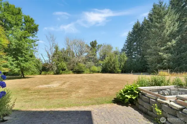 Back patio with a pond, perfect for relaxing or entertaining. The property extends into the trees, offering a peaceful setting with ample space to create your own private trails or woodland retreat.