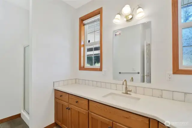 Bright and clean lower bathroom with tile backsplash, and a large windows for natural light. The space features luxury vinyl plank flooring and a separate toilet area for added privacy.