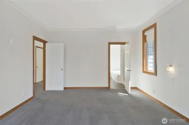 Another angle of the primary suite showcasing wall sconces, dual windows, and access to the en-suite bath. Spacious and serene.