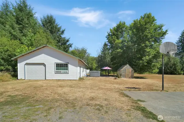 The detached shop sits next to a patio area with hot tub/swim spa, a walk-in greenhouse, and open yard space. Perfect for gardeners and hobbyists alike.