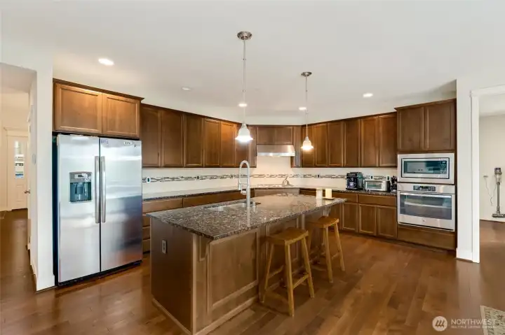 Spacious and efficient, this kitchen is designed for everyday cooking and hosting. Stainless steel refrigerator and double ovens complement the espresso cabinetry and granite surfaces, while the island seating invites connection at the heart of the home.