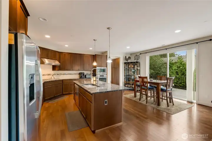 Bright and open chef’s kitchen featuring rich cabinetry, stainless steel appliances, and a large granite island perfect for casual dining or entertaining. The adjoining dining area opens to the back deck through sliding glass doors, ideal for gatherings or summer BBQs.