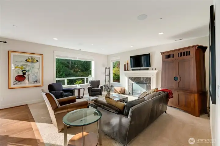Spacious and inviting living room with large picture windows that frame lush greenery outside. The focal point is the gas fireplace with elegant tile surround and a custom mantel, ideal for cozy evenings or entertaining guests in comfort.