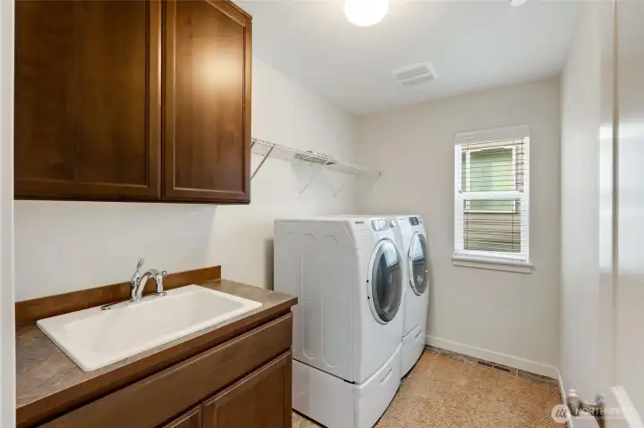 Dedicated upstairs laundry room with front-loading washer and dryer, deep utility sink, and upper cabinetry for storage. Conveniently located with space for folding and organization.