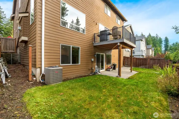 Fully fenced backyard with lush green lawn, patio, and covered deck area above. The lower-level walkout provides easy access from the daylight basement, offering flexible outdoor living and entertaining options.