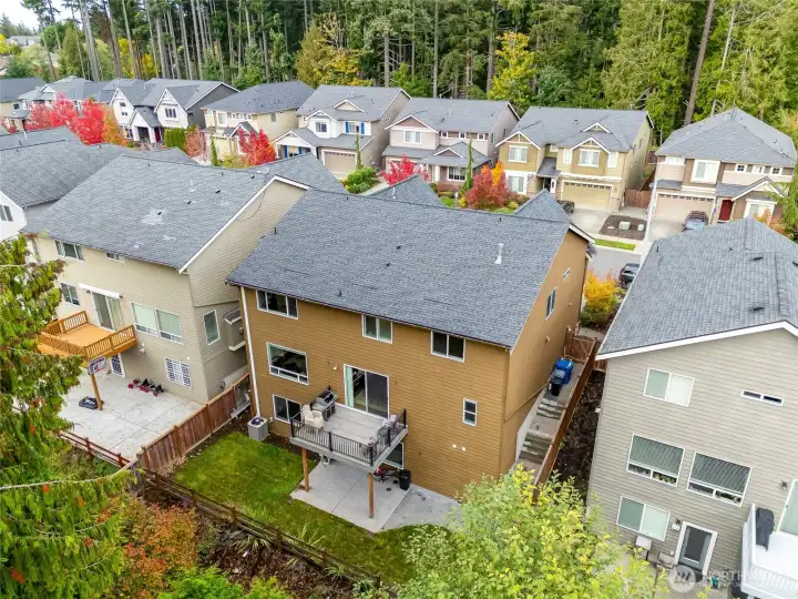 Aerial view from behind the home showing the fenced backyard, outdoor living spaces, and greenbelt backdrop providing privacy and natural scenery.