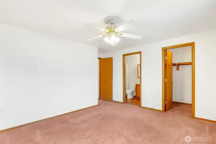 Another view of the primary bedroom, which has a ceiling fan, walk-in closet, and 3/4 bath.