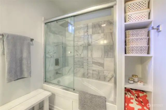 Primary bathtub/shower and built-in storage shelving.