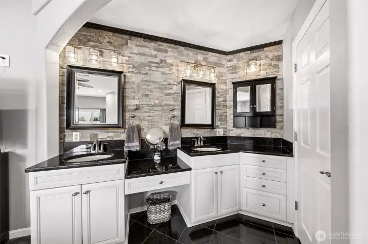 Elegant vanity area off the primary suite with tile accent wall, double vanity and small makeup counter.