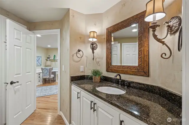 The main level powder room has plenty of storage, hardwood flooring, and beautiful granite countertops.