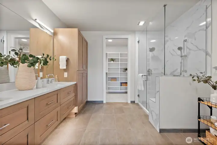 Modern and bright primary en-suite bathroom with neutral tones, double integrated sink vanity, ample drawer storage, enclosed glass shower with built-in bench.