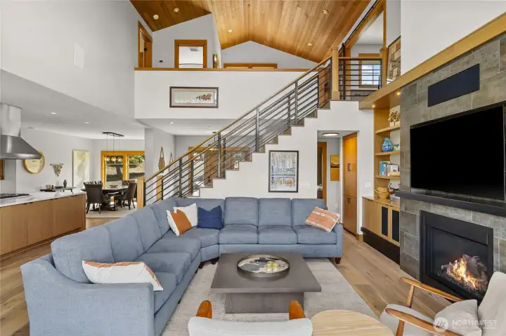 Invited great room featuring a cozy gas fireplace, a staircase leading to the upstairs living area, and a dedicated dining space perfect for entertaining.