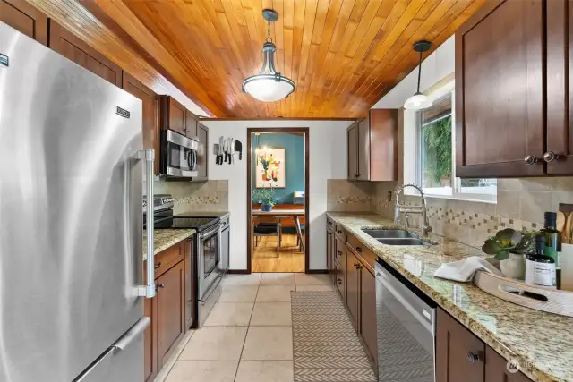 A linear kitchen showcases the beautiful wood planked ceiling, granite counters and ample wood cabinetry.
