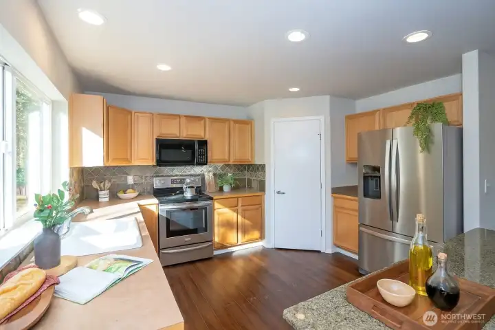 Spacious kitchen designed for easy meal preparation, with an archway that seamlessly connects to the dining and living areas. The kitchen showcases a nearly full-length window that frames beautiful backyard and greenbelt views, filling the space with abundant natural light.