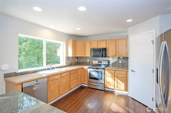 The kitchen showcases a nearly full-length window that frames beautiful backyard and greenbelt views, filling the space with abundant natural light.