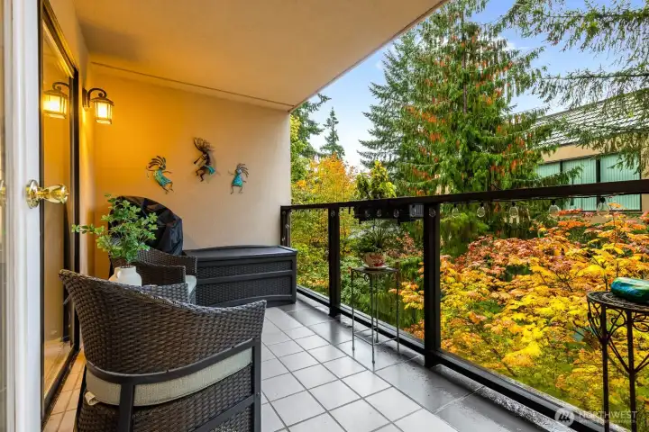 Step from the living room onto a covered balcony surrounded by evergreens and seasonal color.