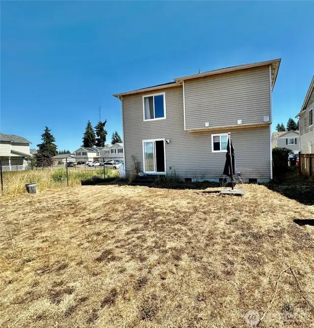Rear view of the home with a partially fenced yard and community parcel next door.