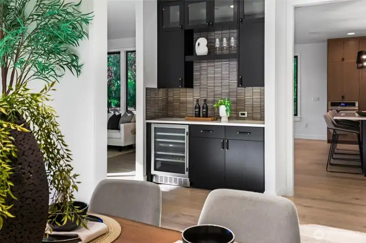 Dramatic dry bar/Butler's pantry with black cabinetry, dual temperature wine refrigerator, glass-front display cabinets with accent lighting and under-cabinet LED lighting, lower cabinetry with pull-out shelves and drawers which are perfect for storing entertaining accessories. The slab countertop serves as a bar or food staging/display area.