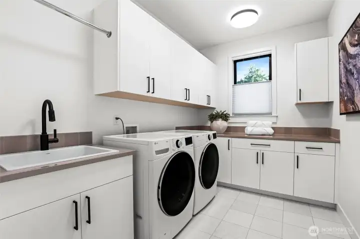 Laundry room lined with cabinets, slab countertops, large utility sink with pull-out faucet, LG® washer and dryer, and a hanging bar.