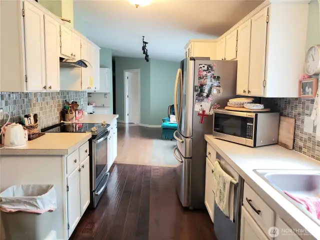Huge Walk Through Kitchen with Tile Back Splash, White Cabinets, Stainless Appliances, Newer Paint and Hard Wood Flooring Looking to the Dining Room Area.