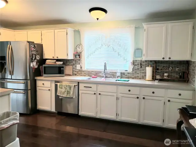 A Different View of the Huge Walk Through Kitchen with Tile Back Splash, White Cabinets, Stainless Appliances, Newer Paint and Hard Wood Flooring.