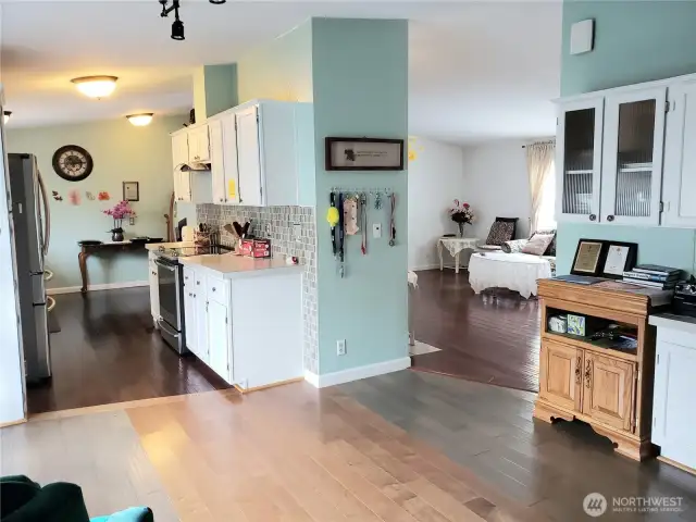 An Over All View from the Dining Room looking at the Huge Walk Through Kitchen with Tile Back Splash, White Cabinets, Stainless Appliances, Newer Paint, Hard Wood Flooring and Living Room.