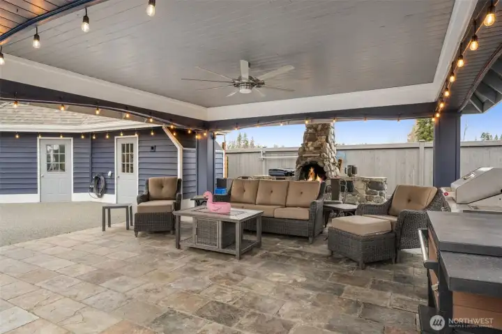 Pool side covered cabana with outdoor fireplace, ceiling fan, and comfortable seating area ideal for year-round entertaining.