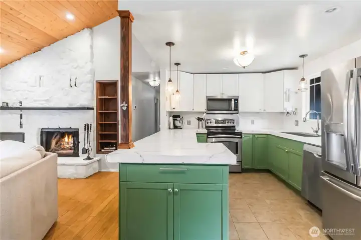 Kitchen open to living room with stone surrounded fireplace with mantle & built in shelving.