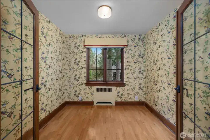 Den - Cheerful wallcovering, divided-light doors, and hardwood floors highlight the home’s distinctive historic charm.