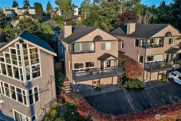 This photo shows the homes' full-length deck with partial cover, glass door entry and below the right-hand garage door with automatic opener and room in front for second car parking.