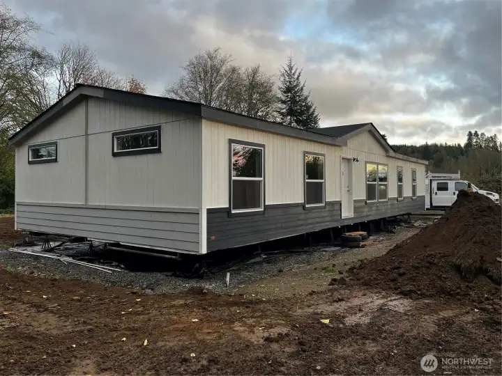 Front of Manufactured home. Front stairs/deck and sidewalk to come. Builder also has plans for concrete curbing, gravel parking pad and hydroseeding soon. Paint still needs finalized on ends of manufactured home.
